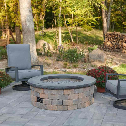 Bronson Block Round Gas Fire Pit Kit Placed at Frontyard with Charcoal Grey Tops and Tumbled Lava Rock