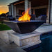 The Malibu Square Fire Bowl in Black Concrete Placed at the Poolside with Cerulean Pebbles with Bullet Burner On plus Match Lit Ignition System