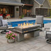 The Outdoor Greatroom Black Uptown Linear Gas Fire Pit Table Installed Near Pool with Clear Tempered Fire Glass Gems and Glass plus Fire Burner On and Glass Wind Guard Installed