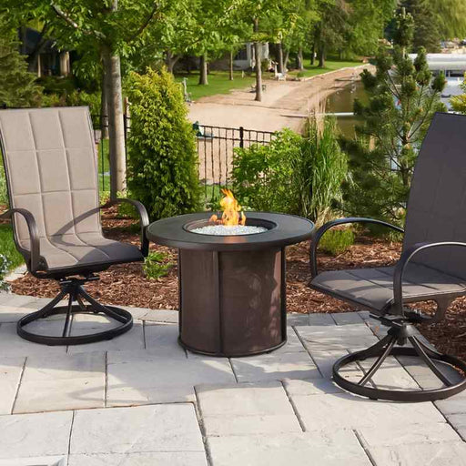 The Outdoor Greatroom Brown Stonefire Round Gas Fire Pit Table Installed at Front Yard  with Clear Tempered Fire Glass Gems plus Fire Burner On