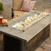 The Outdoor Greatroom Cedar Ridge Linear Gas Fire Pit Table with Clear Tempered Fire Glass Gems, Fire Burner On and Glass Wind Guard