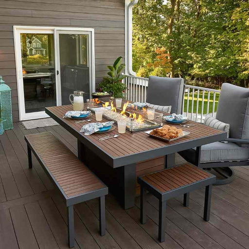 The Outdoor Greatroom Kenwood Linear Dining Fire Pit Table Dinner is ready with Clear Tempered Fire Glass Gems Fire Burner On and Glass Wind Guard Installed