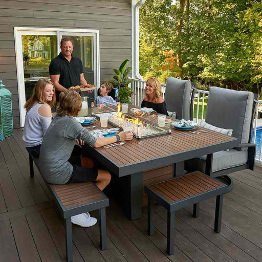 The Outdoor Greatroom Kenwood Linear Dining Fire Pit Table with Family and Clear Tempered Fire Glass Gems Fire Burner On and Glass Wind Guard Installed
