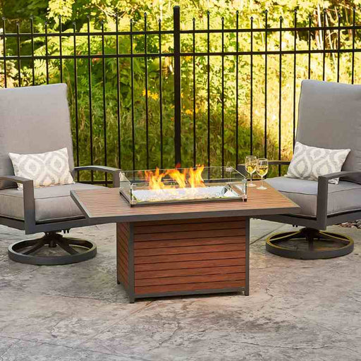 The Outdoor Greatroom Kenwood Rectangular Gas Fire Pit Table place on Guess Waiting Area with Glass Wind Guard installed