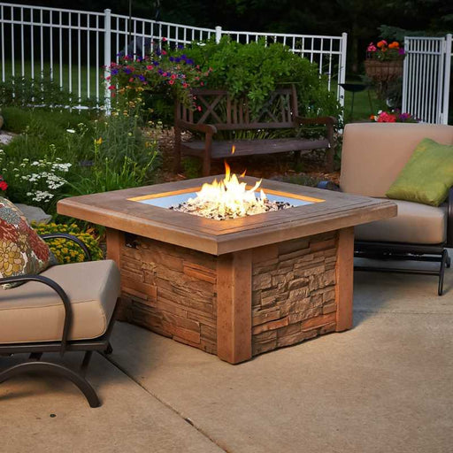 The Outdoor Greatroom Sierra Square Gas Fire Pit Table Placed at Backyard with Clear Tempered Fire Glass Gems and Black Tempered Large Fire Glass Diamonds plus Fire Burner On