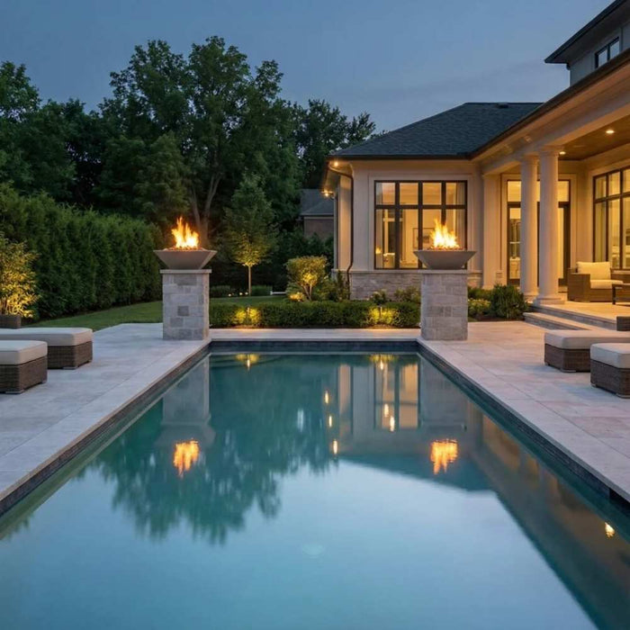 Warming Trends AON Ember square concrete fire bowls in color charcoal with active flames, elevated on matching stone pillars balancing both sides of a luxury rectangular swimming pool area.