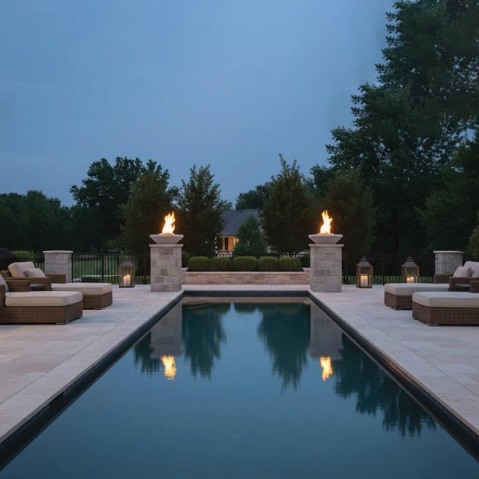 Warming Trends AON Ember square concrete fire bowls in color white with active flames, elevated on matching stone pillars both sides of a luxury rectangular swimming pool area at dusk.