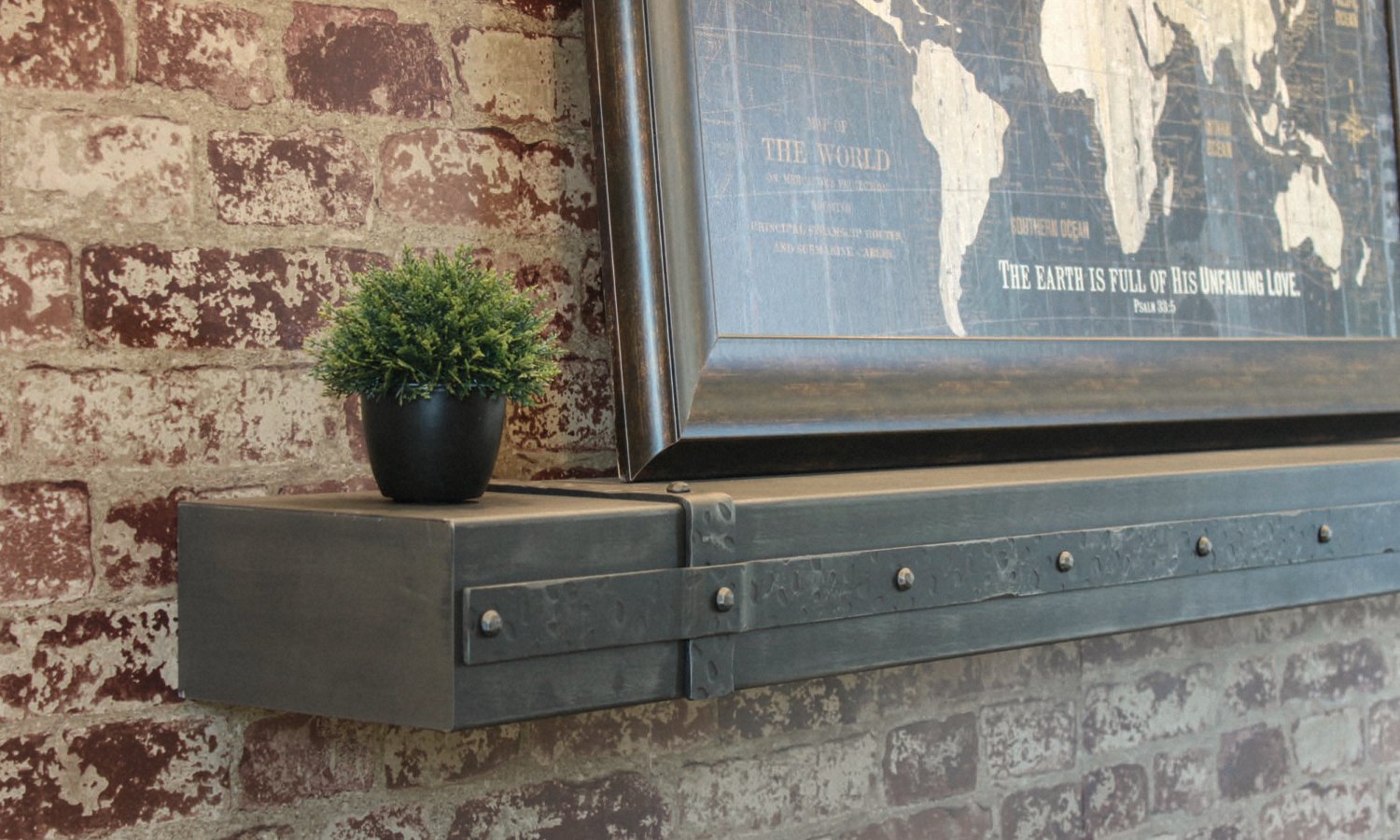 Tight detail of a hand-aged grey mantel shelf with riveted strap banding, mounted on a distressed brick wall.