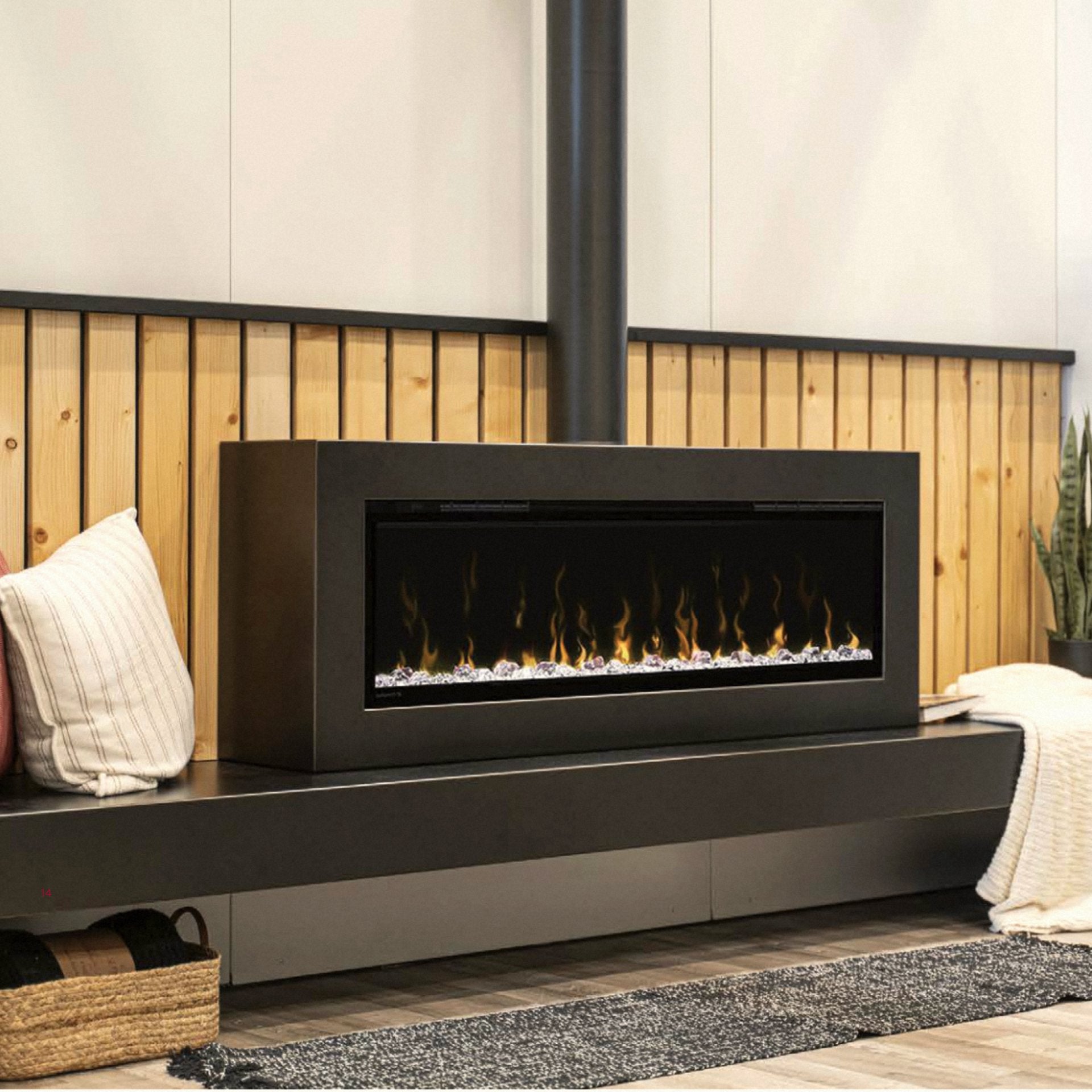 Linear electric fireplace cabinet on a low bench with a warm cedar-slat wall behind, throw pillow and woven basket beside.
