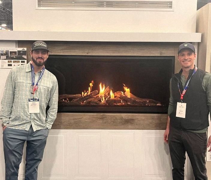 The Torch Guys team standing beside a linear gas fireplace at a builders trade show.